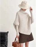 A cream-colored, ribbed-knit turtleneck sweater with wide sleeves and a slightly asymmetrical hem