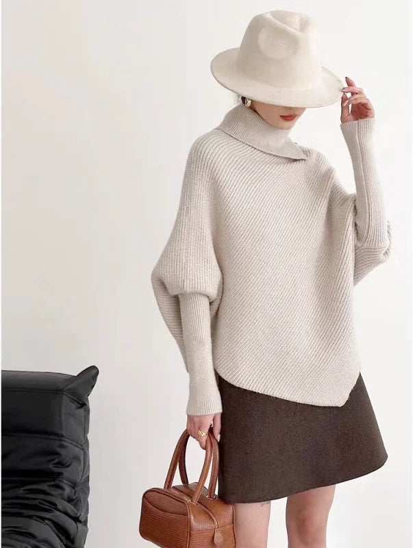 A cream-colored, ribbed-knit turtleneck sweater with wide sleeves and a slightly asymmetrical hem