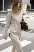 A cream-colored, oversized knit sweater with a high neckline and side slit