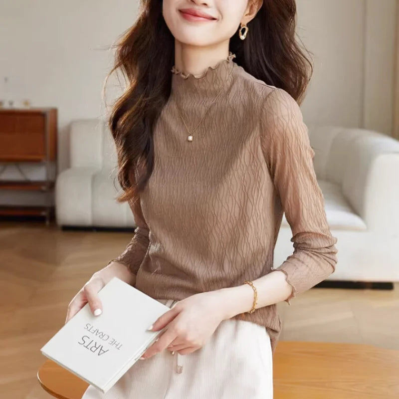 A beige, semi-sheer long-sleeved top with a ruffled high neckline and subtle wavy texture