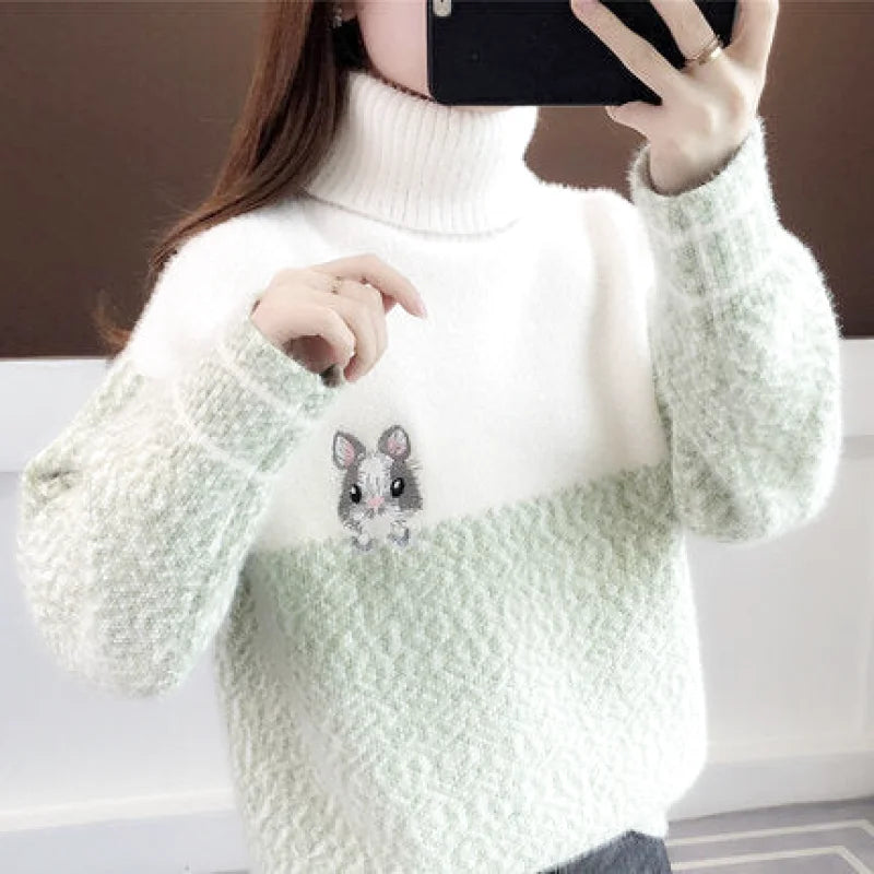 A cozy white and light green turtleneck sweater with a textured knit, featuring an embroidered gray hamster on the chest