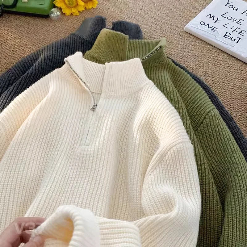 Cream-colored ribbed knit sweater with a half-zip collar and dark green and charcoal gray versions displayed behind it