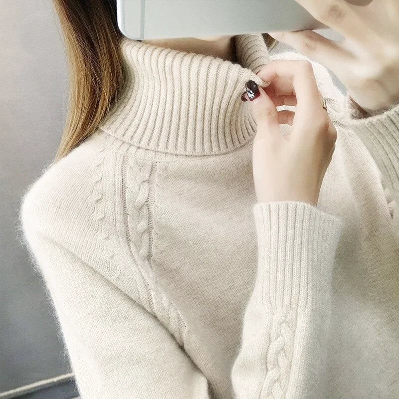 Cream-colored, ribbed turtleneck sweater with a cable-knit pattern across the chest and sleeves