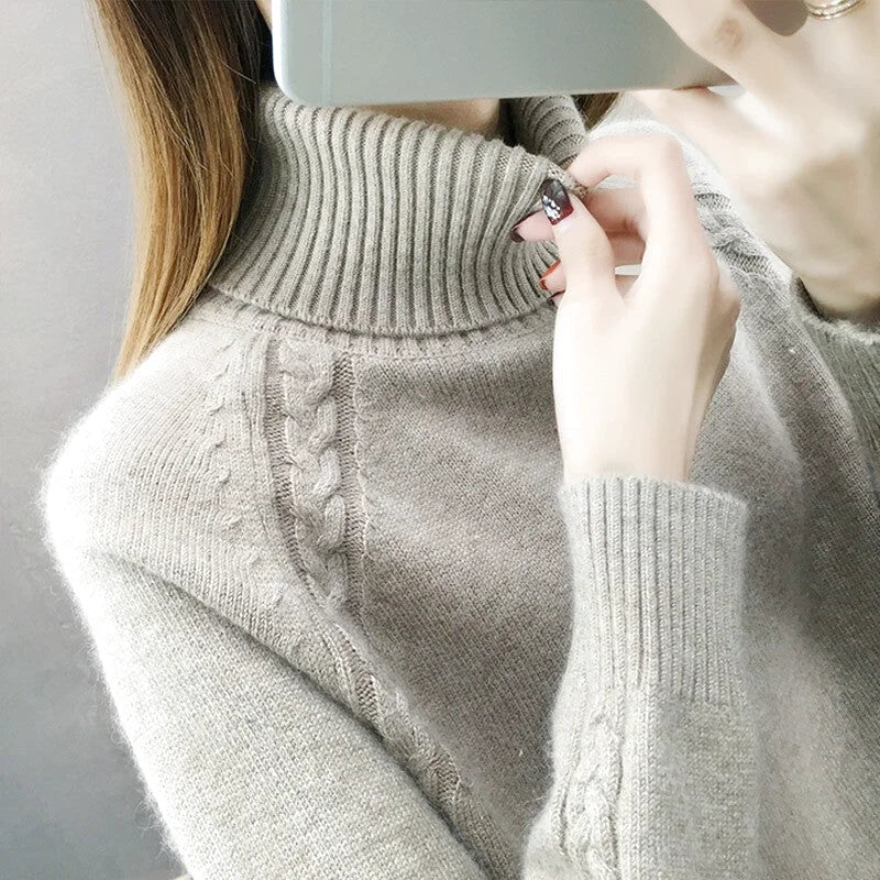 A soft, light gray turtleneck sweater with a ribbed collar and intricate cable-knit detailing along the front
