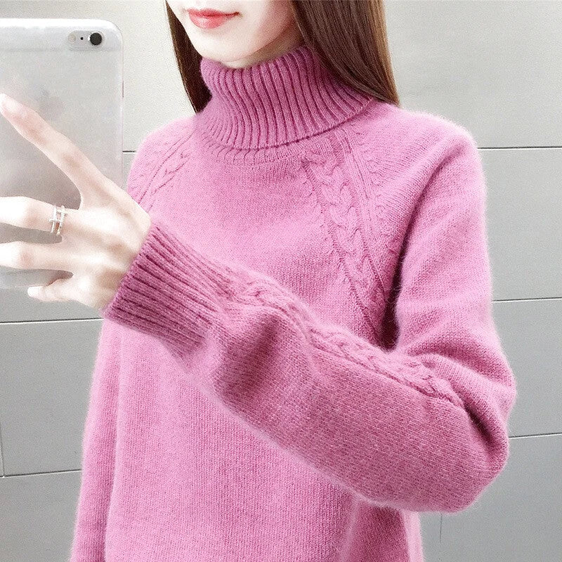 A soft pink turtleneck sweater with a ribbed collar and cuffs, featuring intricate cable-knit patterns along the sleeves