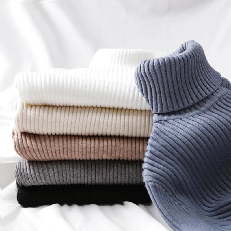 Stack of ribbed turtleneck sweaters in soft neutral tones, including white, beige, taupe, gray, and black